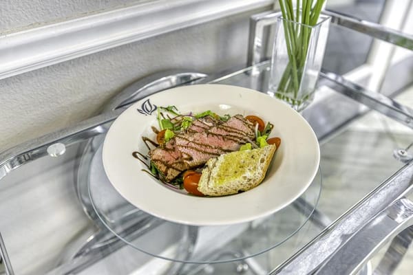 Plate with steak, salad, and bread on a glass table