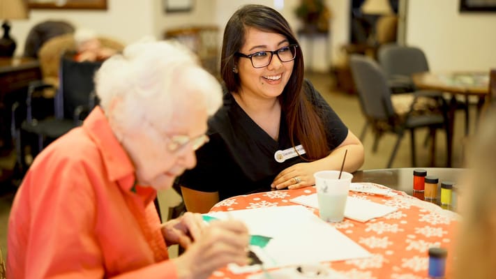 Resident painting with staff member assisting in an activity room