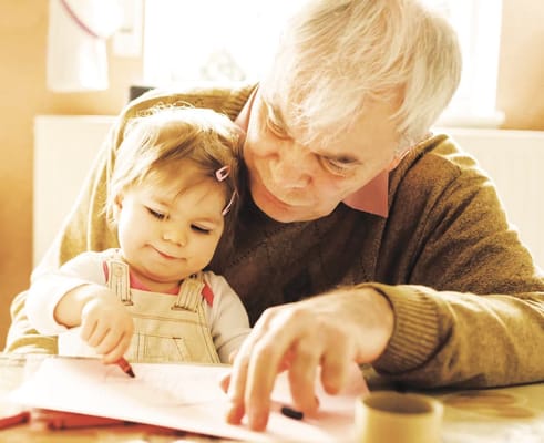 A senior man coloring with a young girl
