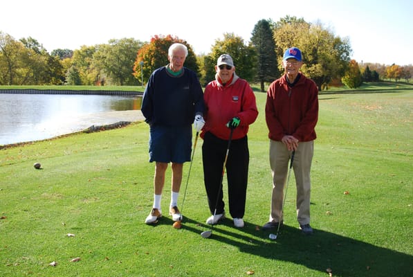 Three seniors playing golf by a picturesque pond