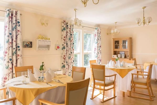 Bright dining room with floral curtains and tables set for meals