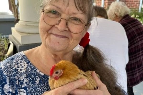 Resident holding a chicken outdoors at Harmony Memory Care