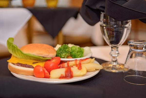 A plate of a cheeseburger, fries, and vegetables at a dining table