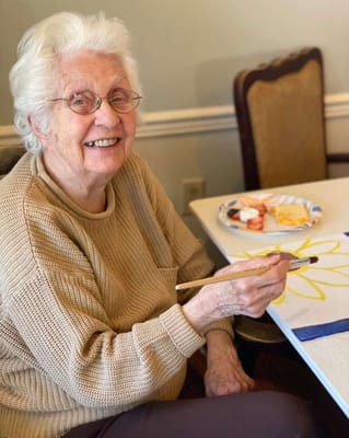 Elderly woman painting at a table in the facility