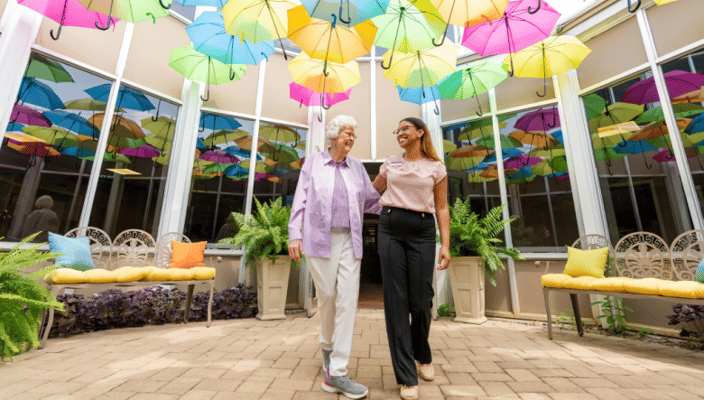 Resident and staff member walking in a brightly decorated area