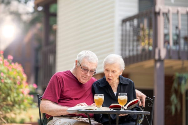 Two seniors reading together outdoors at a small table