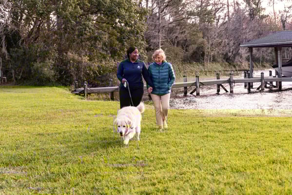Staff member and resident walking a dog by the water