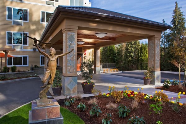 Exterior view of a senior living facility entrance with sculpture and flowers