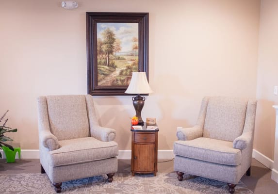 Two comfortable armchairs in a lounge with a lamp and a painting.