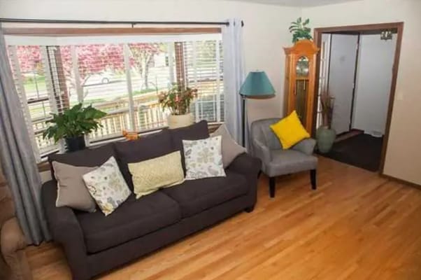 Living room with a sofa, armchair, and large windows letting in natural light.