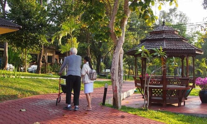 Elderly resident walking in a garden with staff assistance