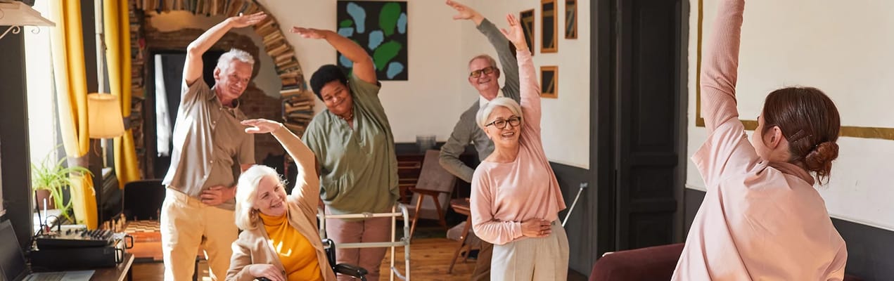Residents and staff engaging in a movement activity in a bright room.