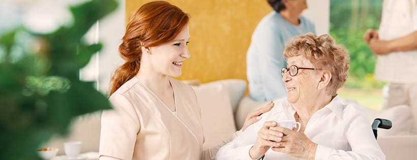 A caregiver smiling and talking with a senior resident in a comfortable setting.