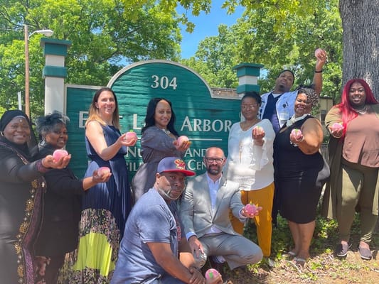 Group of individuals holding peaches in front of East Lake Arbor sign