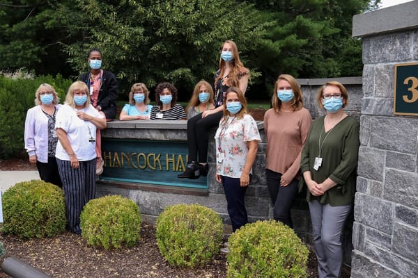A group of staff members posing outside Hancock Hall wearing masks.