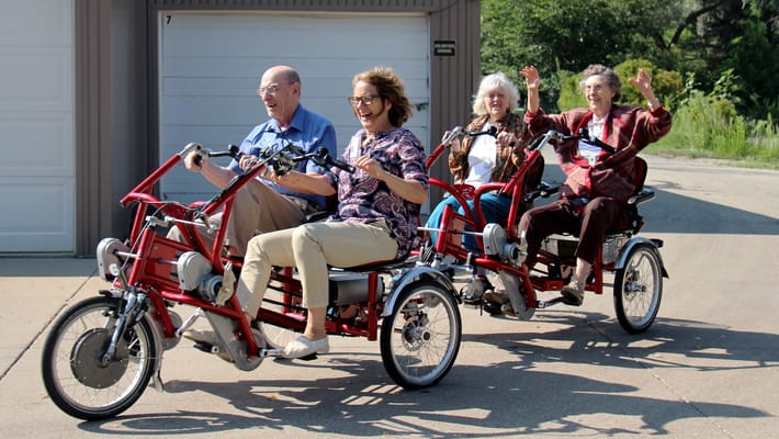 Four residents riding adaptive bikes, smiling and enjoying the outdoors.