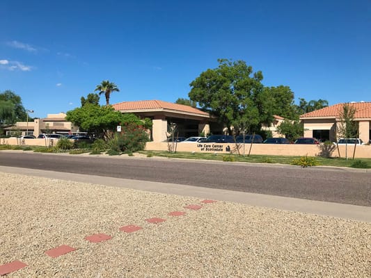 Exterior of Life Care Center of Scottsdale with landscaping and parked cars