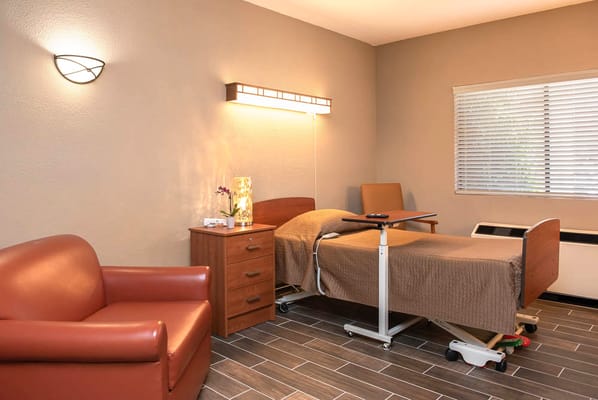 A cozy bedroom with a hospital bed and a chair.