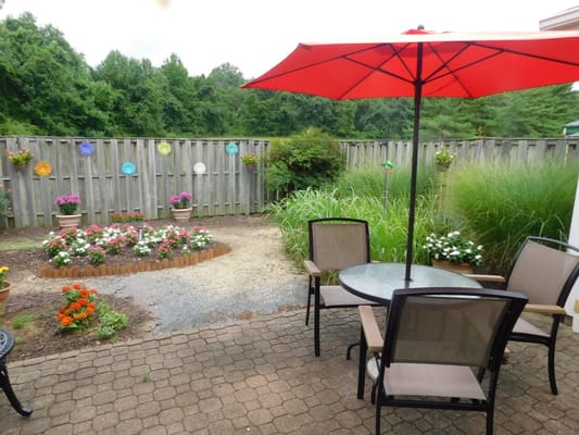 Outdoor seating area with red umbrella and flower garden.
