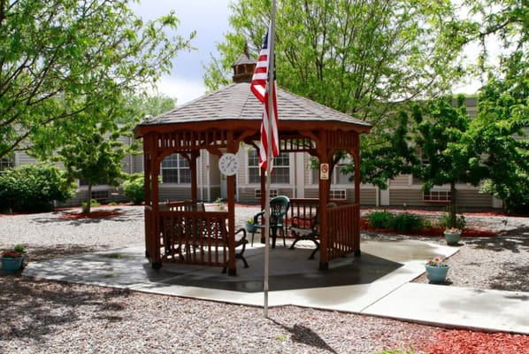 Outdoor gazebo with seating and flag in a landscaped area