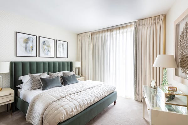 A stylish bedroom featuring a green upholstered bed, decorative pillows, and large windows with sheer curtains.
