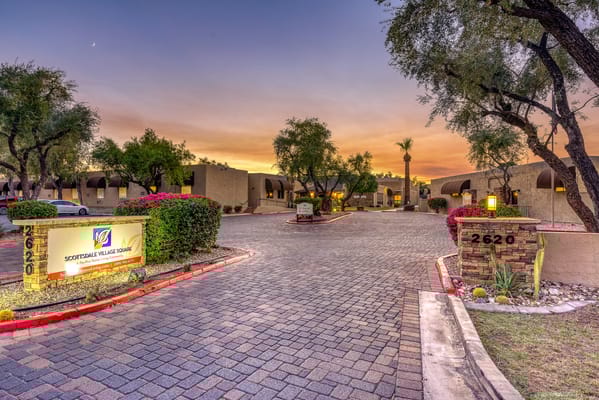 The entrance sign and pathway of Scottsdale Village Square at sunset.