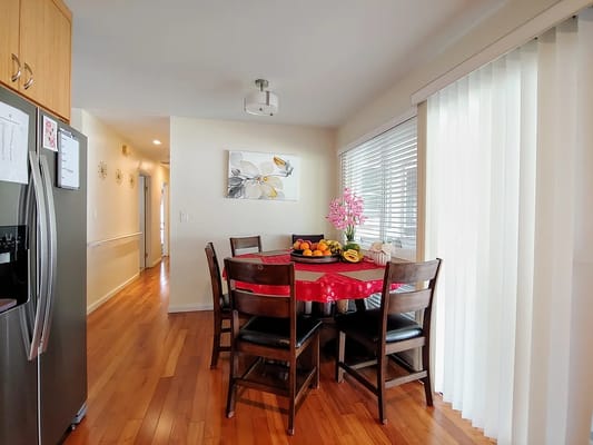 Bright dining area with a wooden table, red tablecloth, and fruit centerpiece.