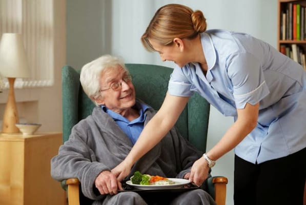 Caregiver serving a meal to a smiling senior resident