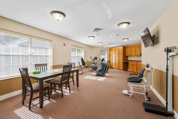 Well-lit fitness room with workout equipment and a dining area