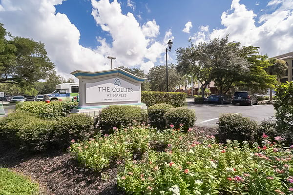 Sign for The Collier at Naples surrounded by greenery and flowers