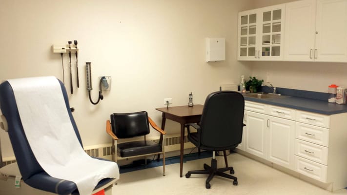 A clean medical examination room with a chair, desk, and medical equipment.