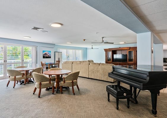 Lounge with seating, dining tables, and a piano in senior living facility