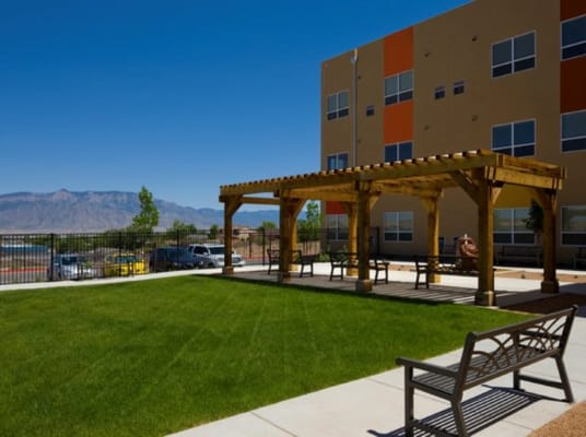 Wooden pergola and benches on a grassy patio area.