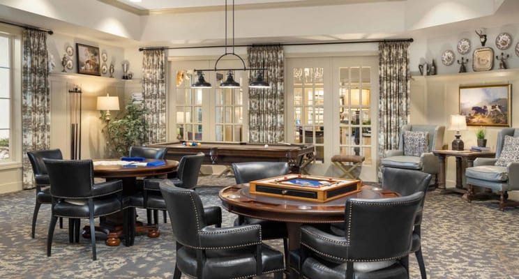 A cozy game room with tables and chairs, featuring a pool table and board games.