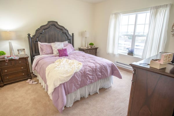 A cozy bedroom featuring a double bed with a purple bedspread, nightstands, and a window