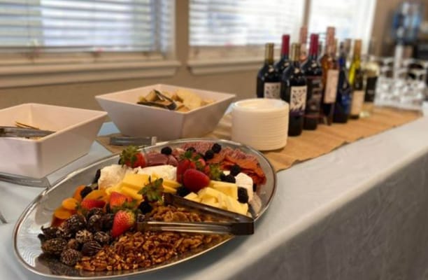 A platter of assorted cheeses, fruits, and nuts with wine bottles in the background.