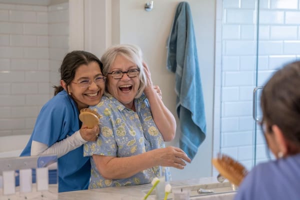 Resident and staff member smiling in a bathroom mirror