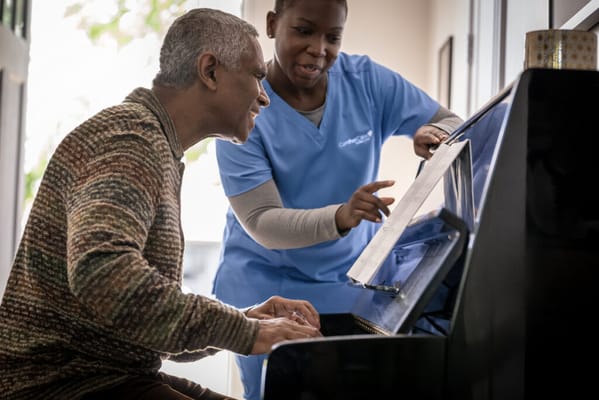 Resident playing piano with a caregiver's assistance
