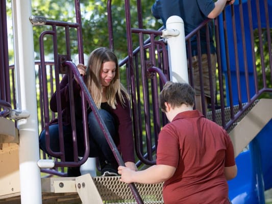 A caregiver assisting a child on playground stairs