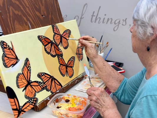 Senior resident painting butterflies on canvas
