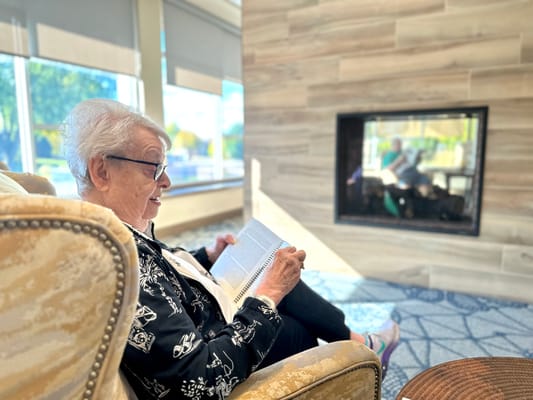 Resident reading in a cozy common area by the fireplace