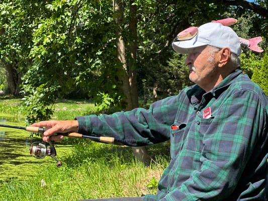 Senior man fishing by a pond in a green space