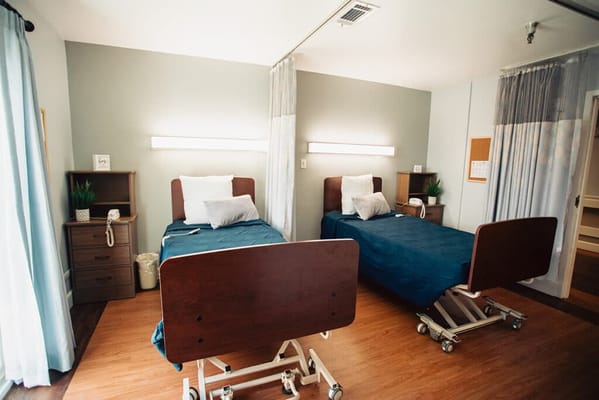 A shared resident room with two beds and medical equipment
