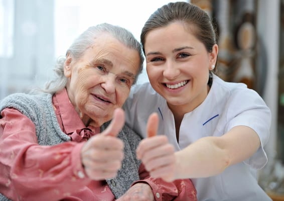 An elderly resident and a caregiver smiling with thumbs up