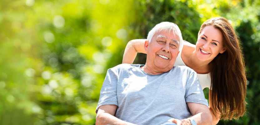 A senior man smiling with a caregiver in a green garden