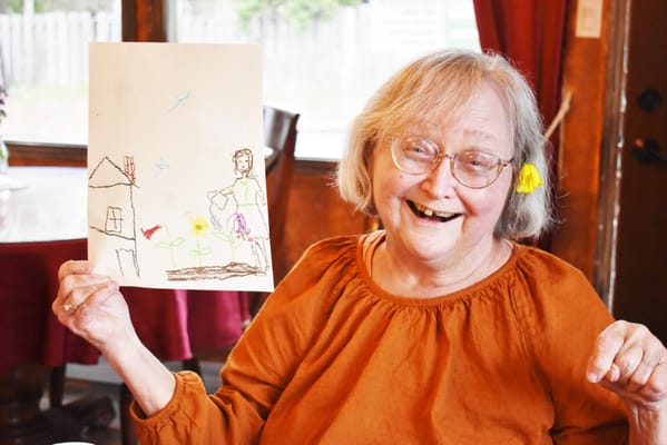 A resident holding a colorful drawing in a warm interior