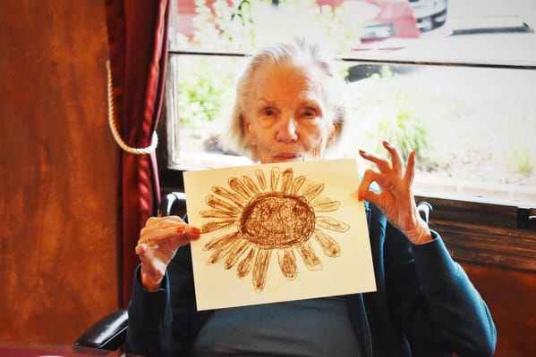 A resident holding a flower drawing in an activity room