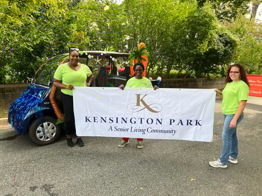 Staff members holding a banner in front of a decorated vehicle