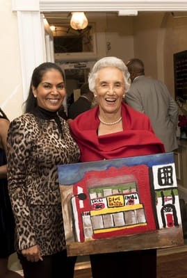 Two women holding a painted artwork at an event