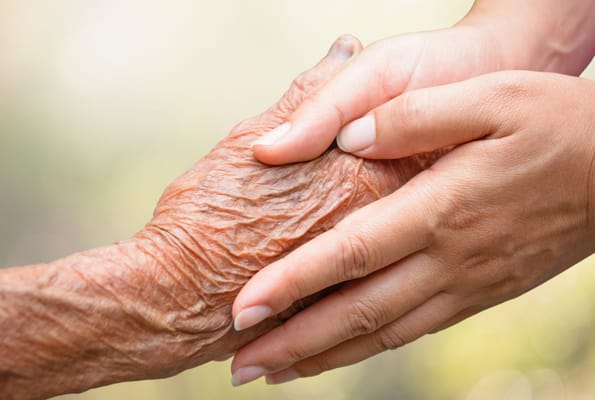 Hands of a caregiver and a senior holding each other